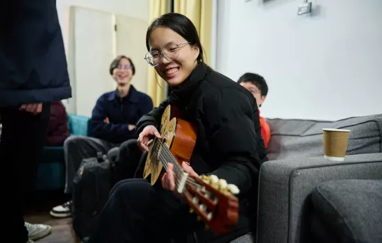 A female student plays the guitar in the JCR during a pizza night.