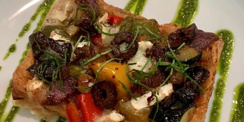 A finished vegan tart drizzled with pesto and plated.