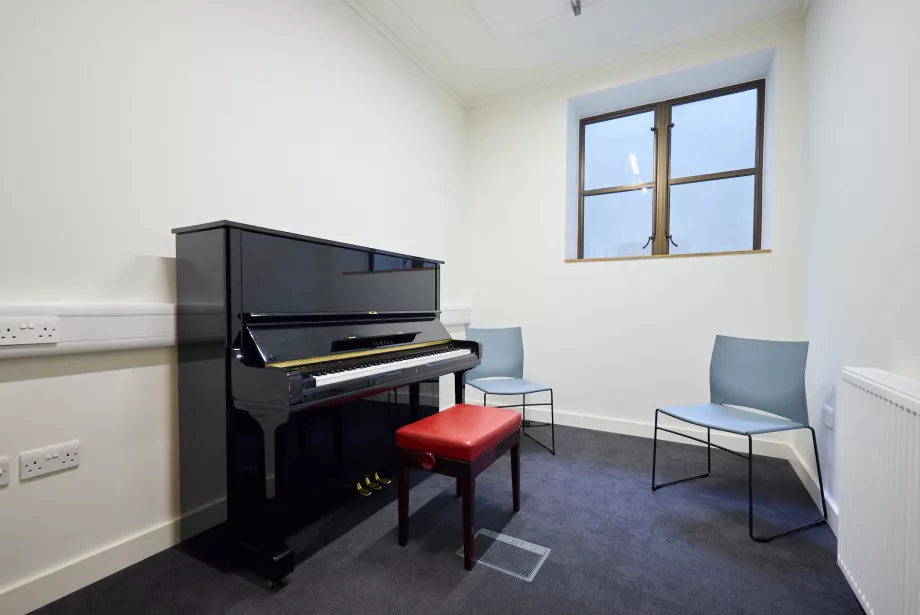 The inside of a music practice room at Trinity college with a piano and bench.